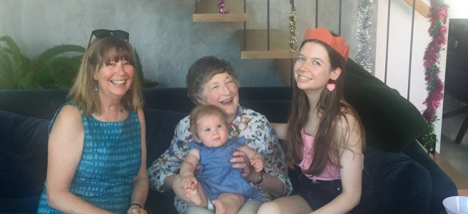 Baby girl, young woman, older woman and elderly woman sitting on a couch smiling