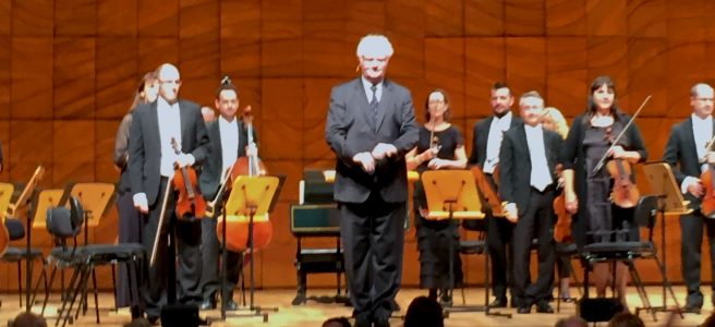 Richard Gill and orchestra standing on stage in front of an audience