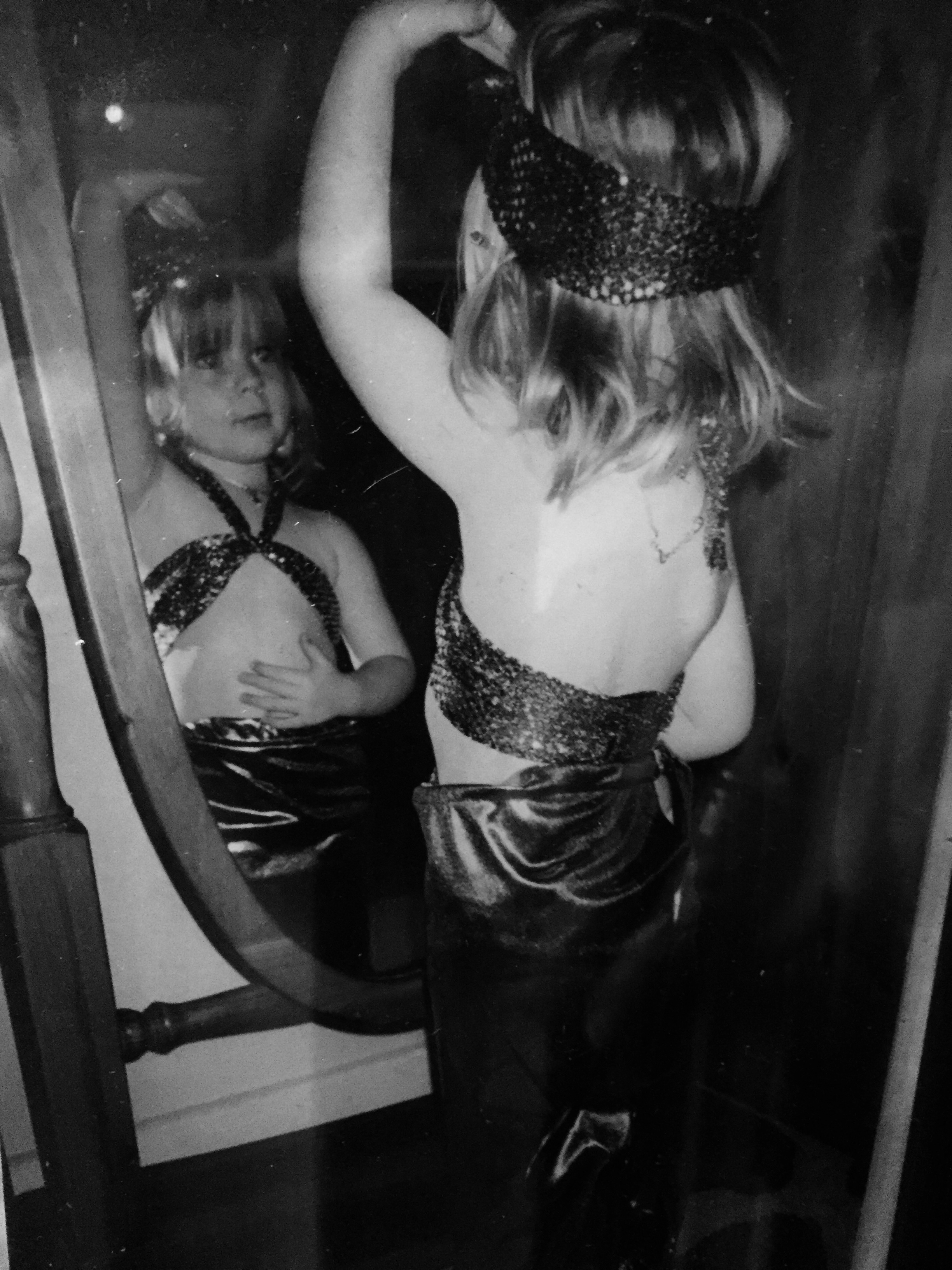 Little girl in mermaid dress ups looking at herself in a full-length mirror