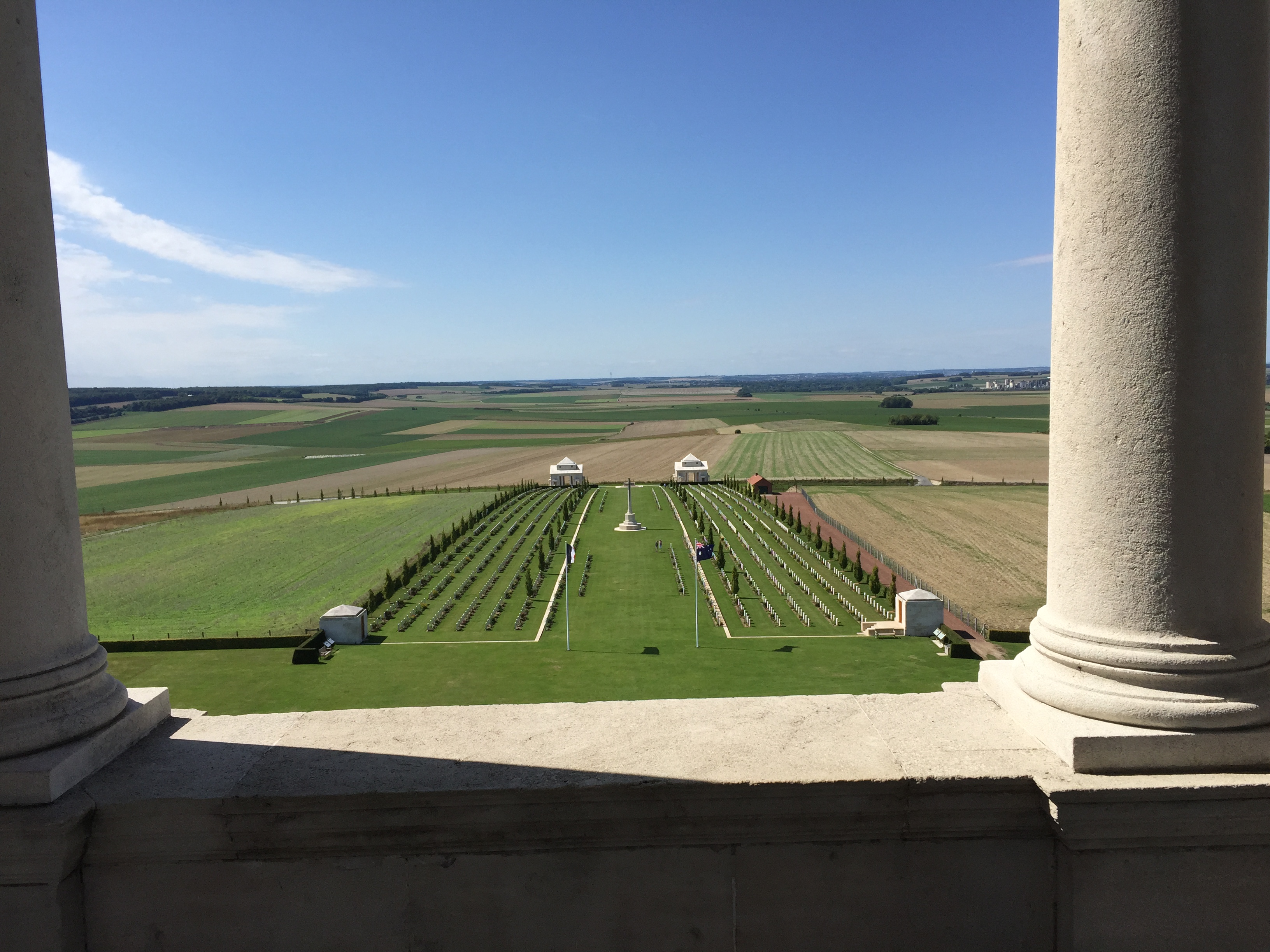 The view looking out on a sunny day with blue skies over rolling hills. In the foreground are rows of headstones on a lawn.