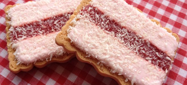 Old-fashioned iced vovos - a rectangular biscuit base topped with a red stripe of jam flanked by pink icing and sprinkled with shredded coconut