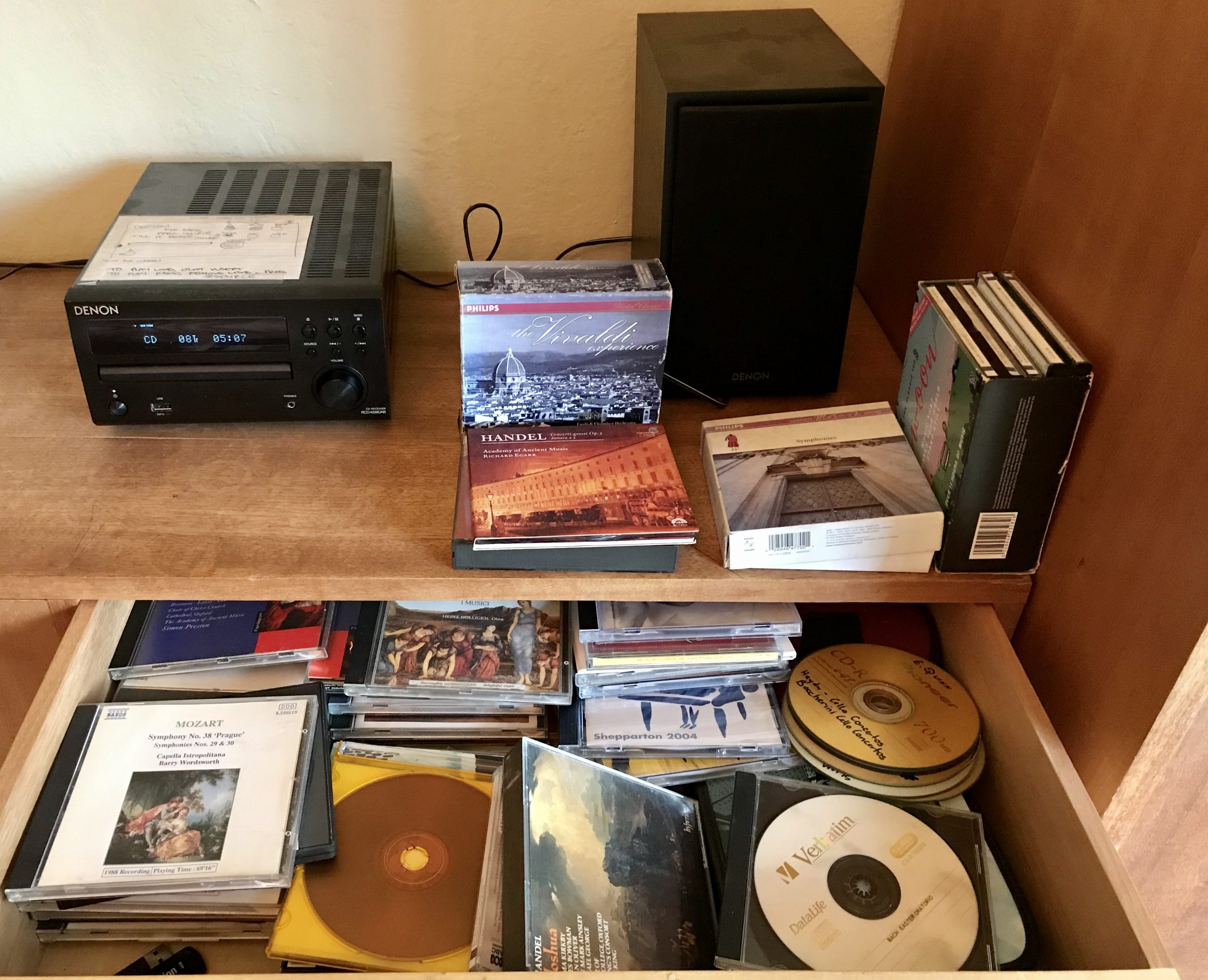 A drawer full of Cds, a CD player and speaker on the bench above it.