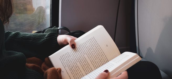 An open book on the lap of someone seated next to a train window