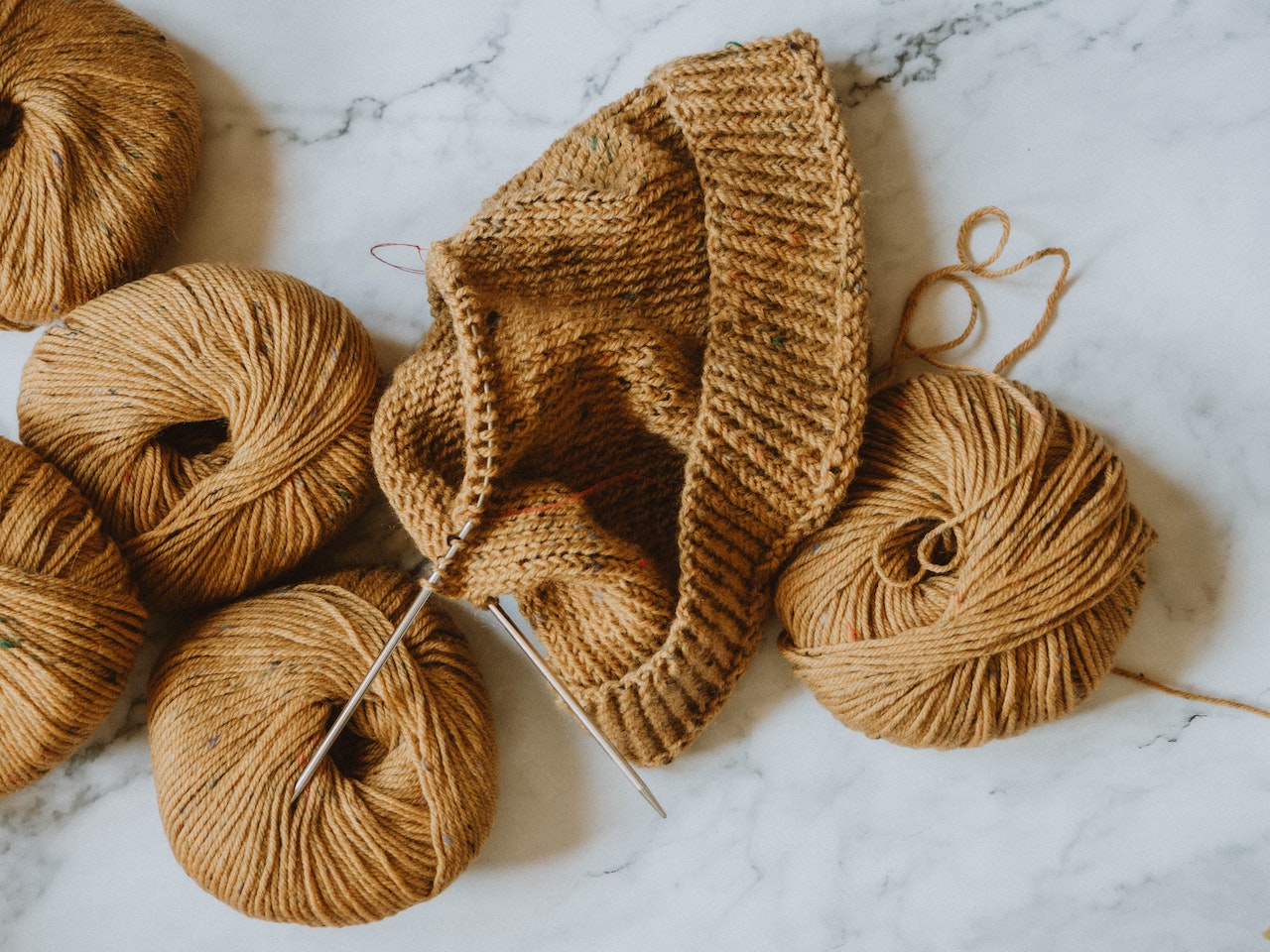 Five balls of wool and an unfinished brown beanie with circular knitting needle